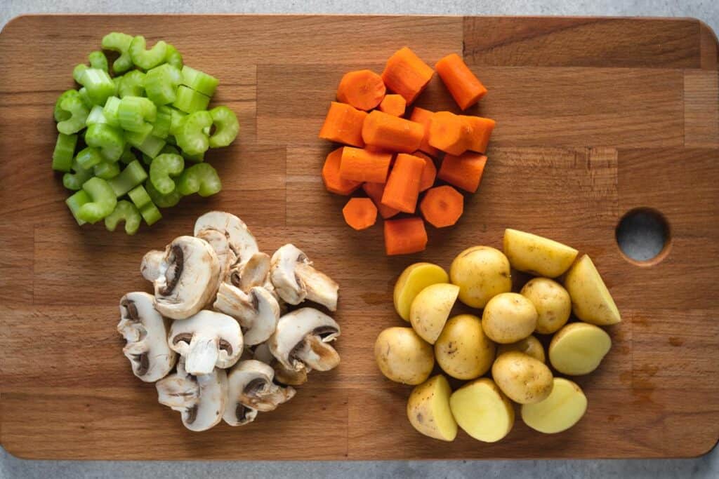 cutting board with chopped up celery, carrots, mushrooms, potatoes