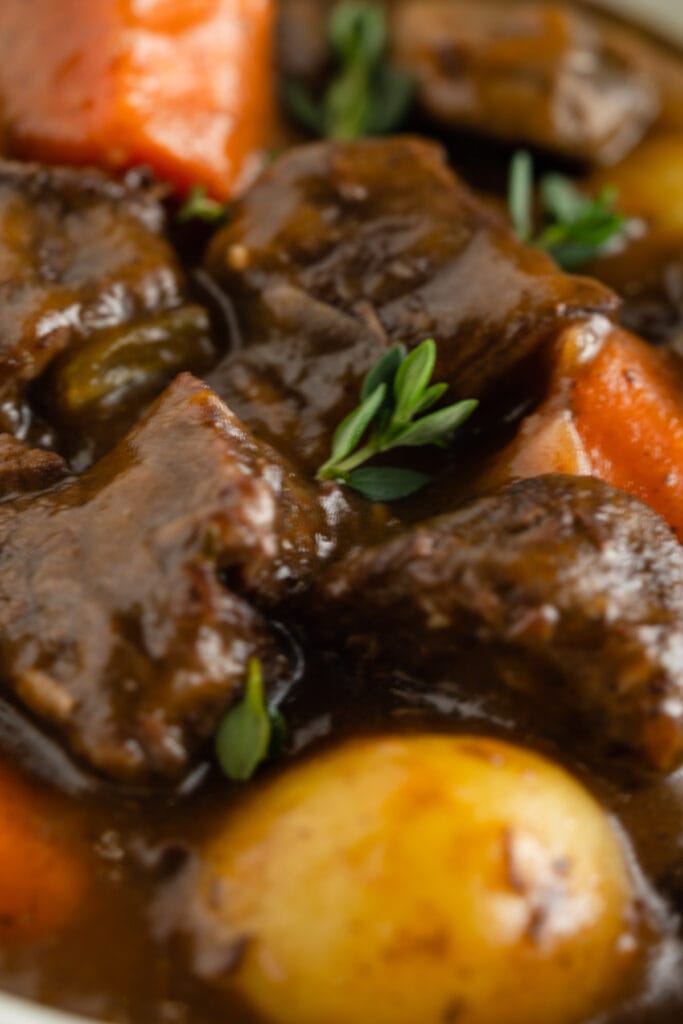 A close up of chunks of beef, carrots, potato and thyme leaves